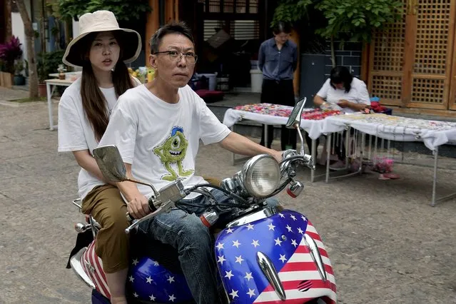 A Chinese couple ride on an electric bike with decals of the American flag, passing by a vendor selling souvenirs on a street in Dali, in southwestern China's Yunnan province on Sunday, July 17, 2022. China's government on Wednesday, July 27, rejected as a “political lie” a report by The Wall Street Journal that Beijing tried to recruit informants in the Federal Reserve system to obtain U.S. economic data. (Photo by Andy Wong/AP Photo)