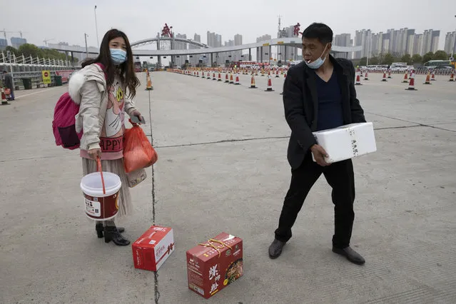 In this Thursday, April 2, 2020, photo, a man assists a woman with her belongings as they cross the expressway gate at the border of Wuhan city in central China's Hubei province. Millions of Chinese workers are streaming back to factories, shops and offices but many still face anti-coronavirus controls that add to their financial losses and aggravation. In Wuhan police require a health check and documents from employers for returning workers. (Photo by Ng Han Guan/AP Photo)