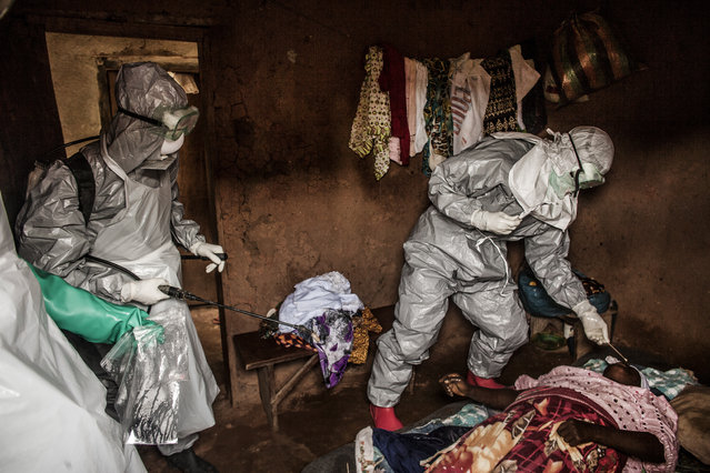 Members of a Red Cross burial team take samples from a  woman suspected of dying of Ebola in the village of Dia on August 23, 2014. So-called “safe burials”, conducted by the International Federation of the Red Cross, are conducted in accordance with rigorous safety procedures. The dead bodies of Ebola victims are extremely infectious. (Photo by Pete Muller/Prime for the Washington Post)