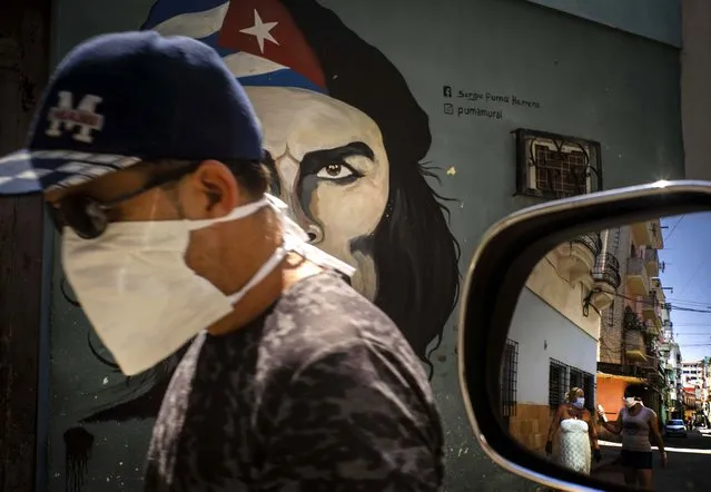 A man wearing a mask walks alongside a mural of Ernesto “Che” Guevara as other pedestrians are reflected in the side-view mirror of a car in Havana, Cuba, Tuesday, April 7, 2020. Cuban authorities are requiring people use masks outside their homes as a measure to help contain the spread of the new coronavirus. (Photo by Ramon Espinosa/AP Photo)