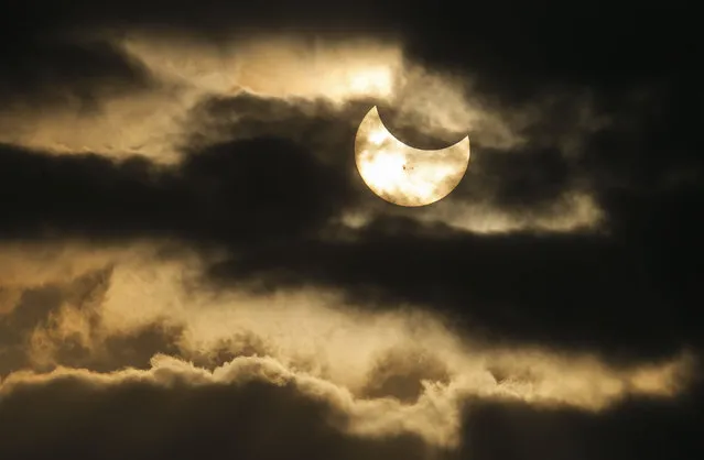 A partial solar eclipse is seen in a break in the clouds during rush hour in downtown Wichita Kan., Thursday, Oct. 23, 2014. (AP Photo/The Wichita Eagle, Travis Heying)
