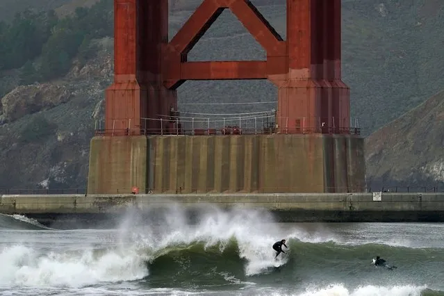 Surfers ride waves in front of a Golden Gate Bridge tower at Fort Point in San Francisco, Friday, January 6, 2023. California weather calmed Friday but the lull was expected to be brief as more Pacific storms lined up to blast into the state, where successive powerful weather systems have knocked out power to thousands, battered the coastline, flooded streets, toppled trees and caused at least six deaths. (Photo by Jeff Chiu/AP Photo)