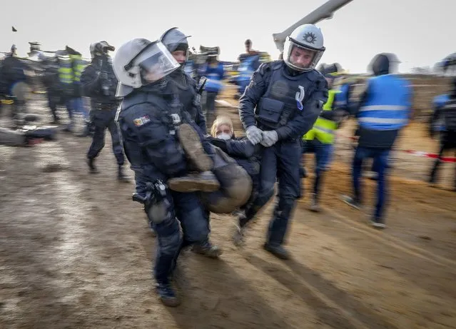 Police officers carry a demonstrator to clear a road at the village Luetzerath near Erkelenz, Germany, Tuesday, January 10, 2023. The village of Luetzerath is occupied by climate activists fighting against the demolishing of the village to expand the Garzweiler lignite coal mine near the Dutch border. (Photo by Michael Probst/AP Photo)