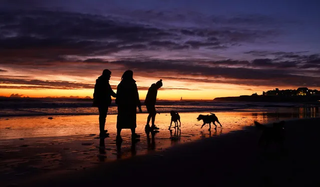 Dog walkers on the beach as the sun rises in Tynemouth on the north east coast on Friday, December 16, 2022. Snow and ice have swept across parts of the UK, with cold wintry conditions set to continue for days. (Photo by Owen Humphreys/PA Images via Getty Images)