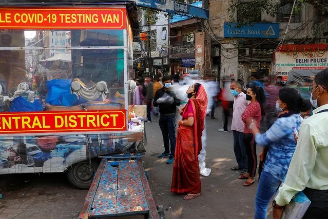 A healthcare worker wearing personal protective equipment (PPE) collects a swab sample from a woman amidst the spread of the coronavirus disease (COVID-19), at a wholesale market, in the old quarters of Delhi, India, November 17, 2020. Picture taken with slow shutter speed. (Photo by Adnan Abidi/Reuters)