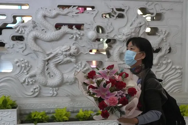 A woman holds a bouquet of flowers upon arriving at the Beijing Capital International Airport in Beijing, Tuesday, March 14, 2023. China will reopen its borders to tourists and resume issuing all visas Wednesday after a three-year halt during the pandemic as it sought to boost its tourism and economy. (Photo by Ng Han Guan/AP Photo)