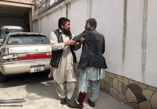 An Afghan man helps an injured man after a bomb blast in Mazar-e-Sharif, the capital city of Balkh province, in northern Afghanistan, Saturday, March 11, 2023.  A bomb exploded on Saturday during an award ceremony for journalists in the city. (Photo by Abdul Saboor Sirat/AP Photo)