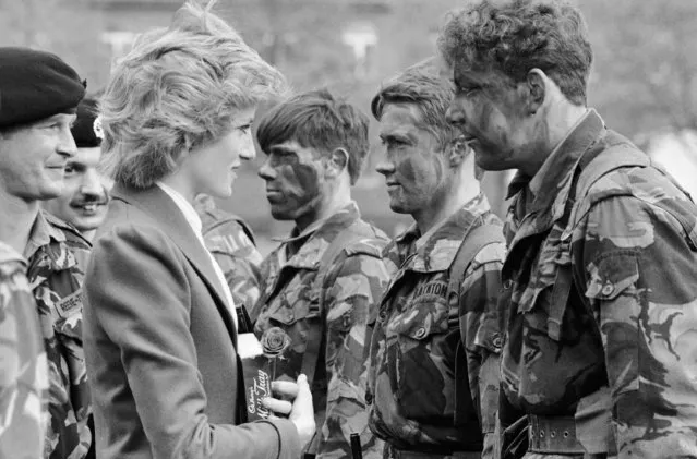 Princess Diana talks with camouflaged-colored combat soldiers when she inspected her Royal Hampshire Regiment in West Berlin on Saturday, October 19, 1985. Princess Diana is a Colonel-in-Chief of the Berlin-based regiment. She holds a box of chocolate and a red rose she was presented with. (Photo by Heribert Proepper/AP Photo)