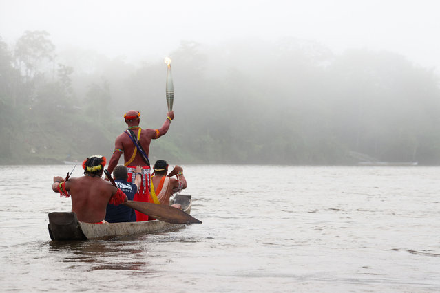 In this handout photograph taken and released by The Paris 2024 press services on June 9, 2024, a torchbearer holds the Olympic Torch on a boat on the Oyapok river during the Olympic torch relay in Camopi, in the French overseas department of Guiana, ahead of the Paris 2024 Olympic Games. The Olympic flame began its journey overseas on June 9 in Guiana, as part of the “Ocean Relay” which will then take it to Reunion Island, French Polynesia, Guadeloupe and Martinique. (Photo by Jody Amiet/Paris 2024/AFP Photo)