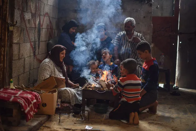 A family warms around a burning firewood on November 23, 2020 in Gaza, Palestine. Palestinians from the poor neighborhood on the outskirts of Khan Yunis camp are preparing for the winter season that comes with a cold snap. (Photo by Yousef Masoud/ZUMA Wire/Rex Features/Shutterstock)