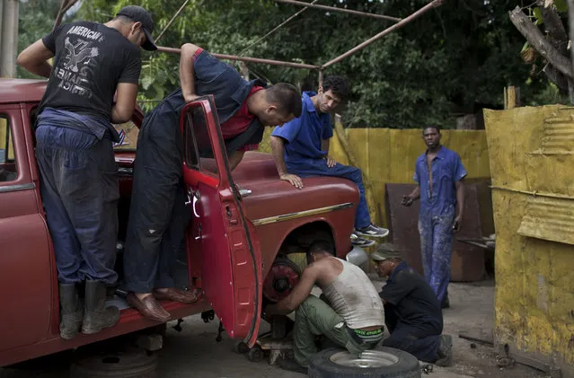 In this October 16, 2014 photo, men repair coil spring of a classic American car in Havana, Cuba. The cars may gleam on the outside, but they're often battered, rolling monuments to ingenuity within. People fabricate parts in crude workshops. (Photo by Franklin Reyes/AP Photo)