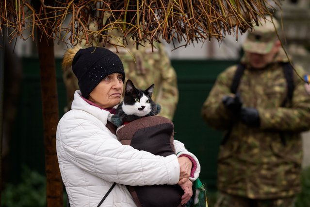 A woman holds Filip the cat as they watch members of Romania's armed forces marching during a full rehearsal for the national day military parade that will take place on December 1, 2025. (Photo by Andreea Alexandru/AP Photo)