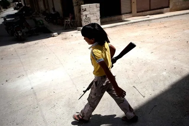 A young Syrian boy holding an old rifle helps fighters belonging to the “Martyrs of Maaret al-Numan” battalion, on June 9, 2013 in the southern Syrian town of Maaret al-Numan. (Photo by Daniel Leal Olivas/AFP Photo)