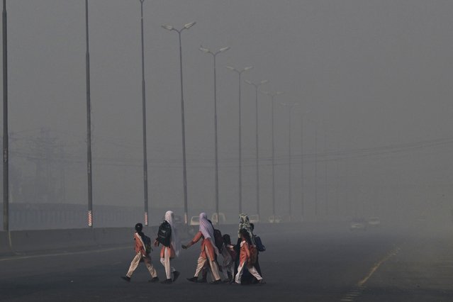 School children cross a road amid dense smog in Lahore on October 27, 2025. (Photo by Arif Ali/AFP Photo)