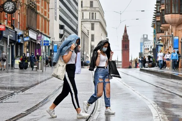 Two women wearing protective face masks cross tram tracks in the rain in Birmingham, central England on August 22, 2020, as Britain's second-city, home to more than one million people, was made an “area of enhanced support”, because of concern about a spike in cases. (Photo by Justin Tallis/AFP Photo)