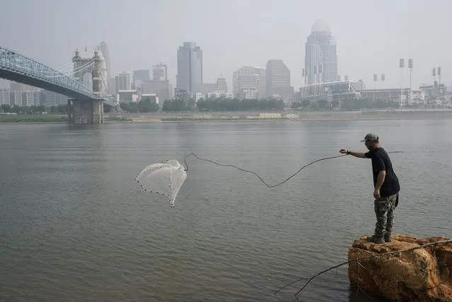 A man tosses a fishing net into the Ohio River as smoke from wildfires is visible over downtown Cincinnati, June 28, 2023. Forecasters say there won’t be large breaks for much of America anytime soon from eye-watering dangerous smoke from fire-struck Canada. (Photo by Joshua A. Bickel/AP Photo)