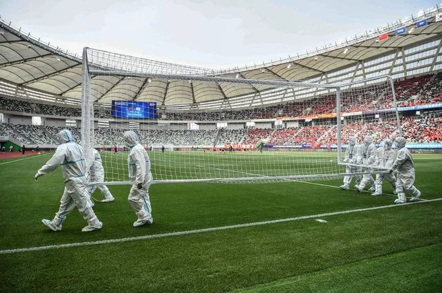 Workers wearing personal protective equipment (PPE) carry a goal post before the qualifying play-off second leg women's football match for the Tokyo 2020 Olympic Games between China and South Korea at Suzhou Olympic Sports Centre Stadium in Suzhou, Jiangsu province on April 13, 2021. (Photo by Hector Retamal/AFP Photo)