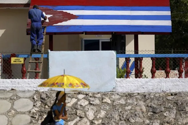 A man touches up a Cuban flag painted on a building as the town prepares for the arrival of the caravan carrying the ashes of Cuba's late President Fidel Castro in Las Tunas, Cuba, December 1, 2016. (Photo by Ivan Alvarado/Reuters)