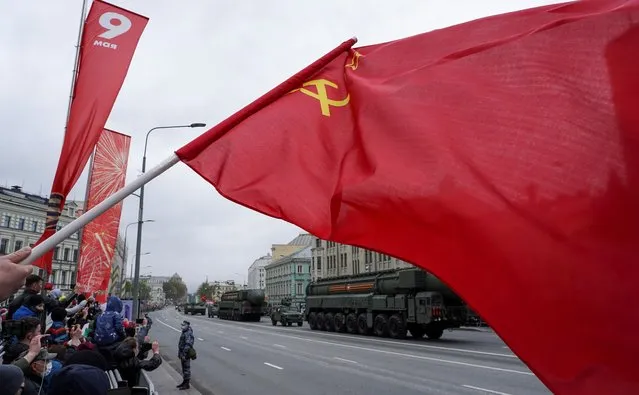 A person waves a Soviet flag as Russian Yars intercontinental ballistic missile systems drive along a street during a military parade on Victory Day, which marks the 76th anniversary of the victory over Nazi Germany in World War Two, in central Moscow, Russia on May 9, 2021. (Photo by Artem Mikryukov/Reuters)