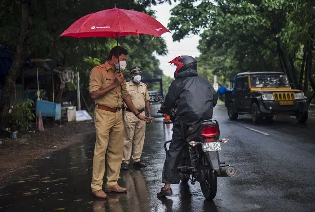 A police officer holds an umbrella to protect himself from the rain as he enforces a lockdown to curb the spread of the coronavirus in Kochi, Kerala state, India, Sunday, May 16, 2021. (Photo by R.S. Iyer/AP Photo)