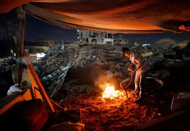 A Palestinian man lights a fire amid the rubble of his house which was destroyed by Israeli air strikes during the Israel-Hamas fighting, in Gaza Strip, May 23, 2021. (Photo by Ahmed Jadallah/Reuters)