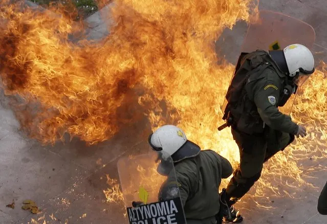 Riot policemen try to avoid a petrol bomb thrown by protesters during a 24-hour nationwide general strike in Athens, Thursday, February 4, 2016. Clashes have broken out between Greek police and youths throwing fire bombs and stones, as tens of thousands of people march through central Athens to protest planned pension reforms. (Photo by Thanassis Stavrakis/AP Photo)