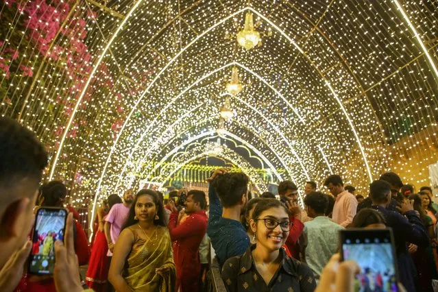 People pose for pictures under a light tunnel as streets are lit up with lanterns and lights on the occasion of the Diwali festival in Mumbai, India on November 12, 2023. Diwali, the Hindu festival of lights, symbolizes the victory of good over evil and commemorates Lord Rama's return to his kingdom, Ayodhya, after completing a 14-year exile. (Photo by Divyakant Solanki/EPA/EFE)