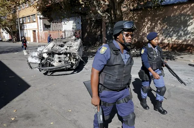 Police officers walk past a car that was burnt overnight in Johannesburg, April 17, 2015. (Photo by Siphiwe Sibeko/Reuters)