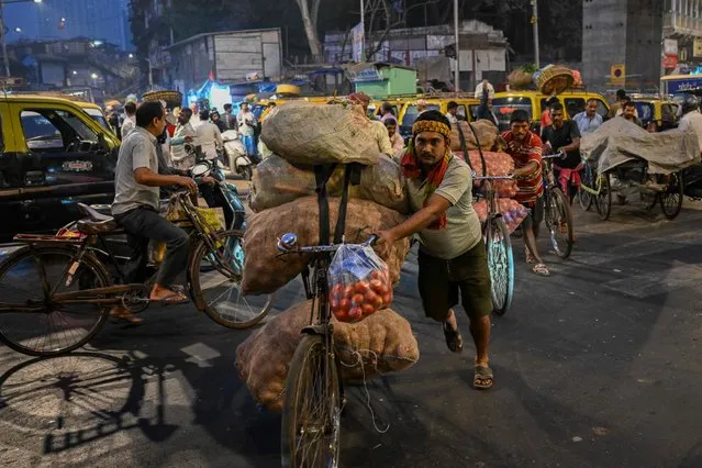 Daily wage workers transport sacks of vegetables on their bicycles during early morning at a wholesale market in Mumbai on February 1, 2024. (Photo by Punit Paranjpe/AFP Photo)