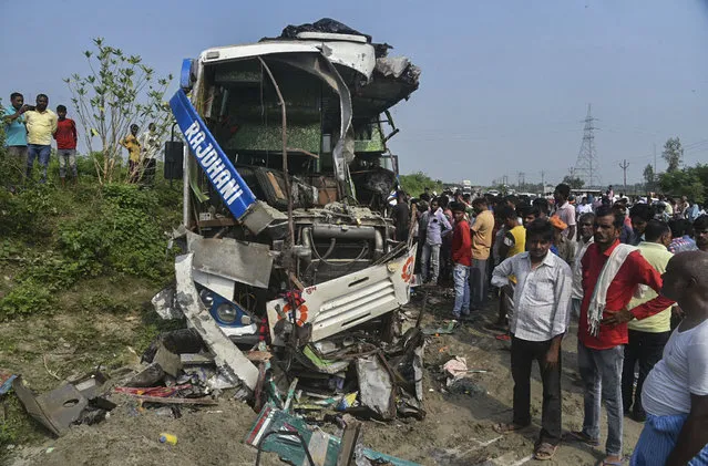 People stand near the wreckage of a bus that collided with a truck in Barabanki district, Uttar Pradesh state, India, Thursday, October 7, 2021. Nearly a dozen people were killed and several suffered critical injuries. (Photo by AP Photo/Stringer)