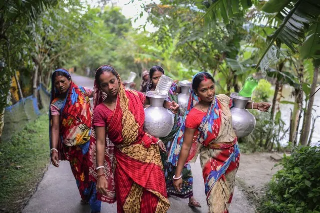 Women walk homewards carrying drinking water in Bonbibi Tala in Satkhira, Bangladesh on  October 5, 2021. Each woman walks up to four kilometer (2.4 miles) daily. Salinity in soil has increased by 26% over the past 35 years, and continues to do so every year in this region. Officials working in the Shyamnagar region admit that paucity of funds was preventing the government from building new desalination plants that would convert saltwater to fresh water. (Photo by Mahmud Hossain Opu/AP Photo)