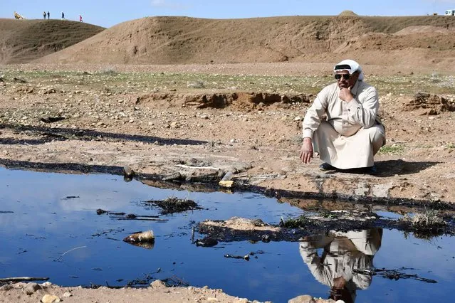 An Iraqi farmer squats and checks an oil spill into an agricultural land in the region of Hamrin, north of Tikrit, in the province of Salaheddin, on February 19, 2024. Oil spills in Iraq – a country ravaged by decades of conflict, corruption and decaying infrastructure – have contaminated farmland in the northern province, especially during the winter rains. (Photo by Abdel Khalek Azzawi/AFP Photo)