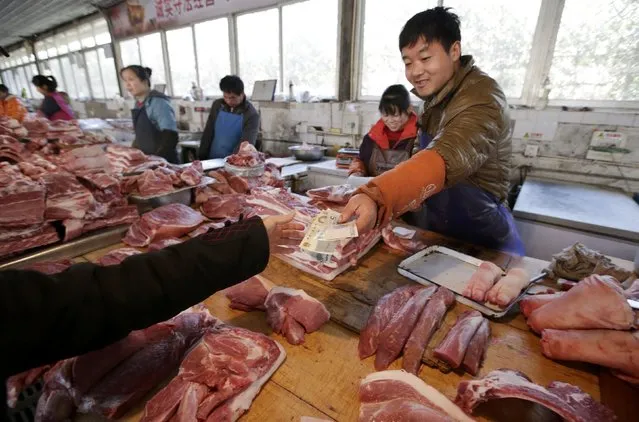 A butcher selling pork returns change to a customer at a market in Beijing, China, March 25, 2016. (Photo by Jason Lee/Reuters)