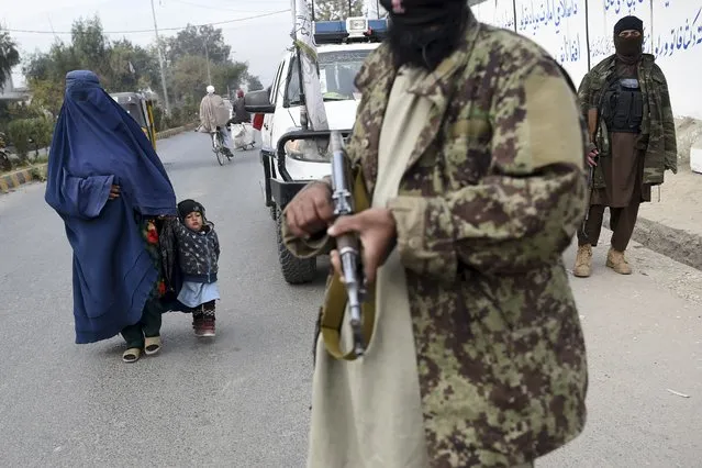 A woman wearing a burqa and a child walk past Taliban fighters along a roadside in Jalalabad on December 12, 2021. (Photo by Wakil Kohsar/AFP Photo)