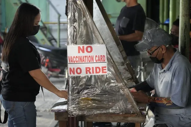 A woman stands beside a sign to remind passengers to show their vaccination card before riding at a jeepney terminal in Quezon city, Philippines on Monday, January 17, 2022. People who are not fully vaccinated against COVID-19 were banned from riding public transport in the Philippine capital region Monday in a desperate move that has sparked protests from labor and human rights groups. (Photo by Aaron Favila/AP Photo)
