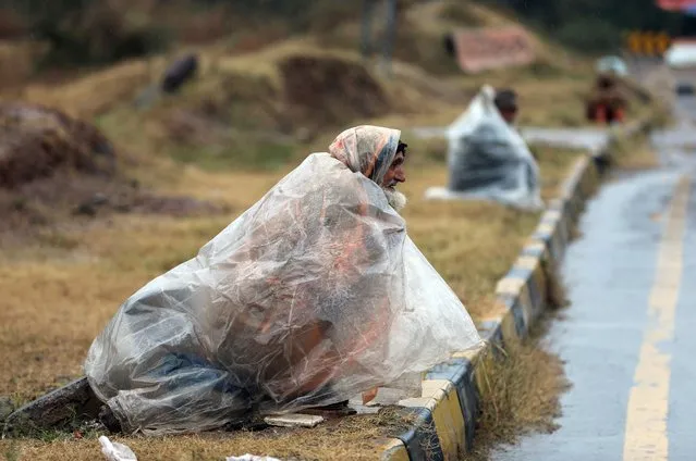 Men wait to receive alms as they cover themselves with plastic sheets in a rain in Islamabad, Pakistan, Wednesday, January 5, 2022. (Photo by Rahmat Gul/AP Photo)