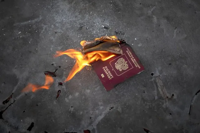 Protesters burn a Russian passport to demonstrates against Russian attacks in Ukraine in front of the Russian embassy in Vilnius, Lithuania, Thursday, February 24, 2022. Russian troops launched a wide-ranging attack on Ukraine on Thursday, as President Vladimir Putin cast aside international condemnation and sanctions and warned other countries that any attempt to interfere would lead to “consequences you have never seen”. (Photo by Mindaugas Kulbis/AP Photo)
