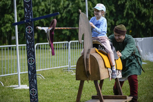 A member of a historic club pushes a wooden horse with a child depicting a horse fight during a festival dedicated to the Day of Russia in St. Petersburg, Russia, Wednesday, June 12, 2024. The Day of Russia is celebrated annually on June 12. (Photo by Dmitri Lovetsky/AP Photo)