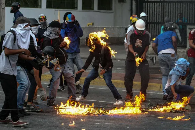 Protesters attempt to handle Molotov cocktails during an opposition demonstration in Caracas, Venezuela, 22 May 2017. Workers in the Venezuelan health sector rallied in favor and against the process of a new National Constituent Assembly, called by President Maduro to overcome the current crisis, on day 52 of mobilizations that are shaking the country. Recent demonstrations left at least 50 dead, according to figures from the authorities and the opposition. (Photo by Cristian Hernandez/EPA)