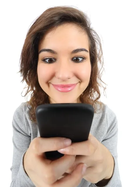 Wide angle view of a pretty teenage girl happy with a smartphone. (Photo by Antonio Guillem/Alamy Stock Photo)