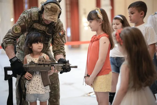 A girl poses with a weapon at a stand set up by Romania's army special forces at the Palace of the Parliament, the second largest administrative building in the world after the Pentagon, as people took the opportunity to visit it for free on International Children's Day in Bucharest, Romania, Wednesday, June 1, 2022. More than fifteen thousand children and adults visited the communist era building, also known as the House of the People, according to the organizers of the event. (Photo by Vadim Ghirda/AP Photo)
