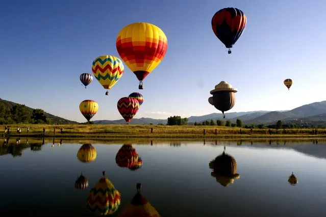 Balloons fly in the sky as their reflections are cast down onto Bald Eagle Lake during the 36th Annual Hot Air Balloon Rodeo in Steamboat Springs, Colorado on July 9, 2017. (Photo by Jason Connolly/AFP Photo)
