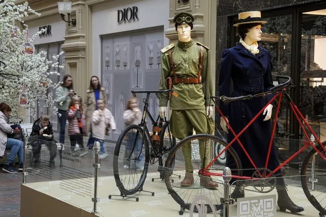 Visitors with their children walk inside the GUM department store with a Dior boutique closed due to sanctions along an installation of a history of cycling in Russia, in Moscow, Russia, Tuesday, May 31, 2022. As Russia's military operation in Ukraine is entering its 100-day anniversary, life in Moscow and St. Petersburg remains largely normal, even as many Western retailers have left Russia. (Photo by Alexander Zemlianichenko/AP Photo)