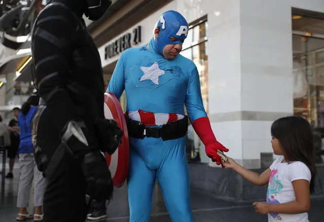 In this Monday, May 22, 2017 photo, a young tourist tips Justin Harrison, wearing a homemade Captain America costume, and Harrison's roommate, Reginald Jackson in a Black Panther costume after taking pictures with them on Hollywood Boulevard in Los Angeles. While the Hollywood we see in film is a place of glamour and beautiful celebrities, the cast of superheroes filling Hollywood Boulevard is frequently anything but. Many are people struggling to make a buck as they pursue their dream of stardom. (Photo by Jae C. Hong/AP Photo)