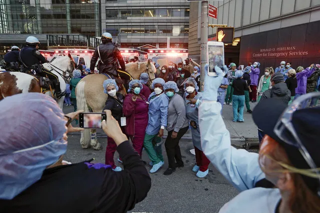 Medical workers pose for photographs as police officers and pedestrians cheer for them outside NYU Medical Center Thursday, April 16, 2020, in New York. (Photo by Frank Franklin II/AP Photo)
