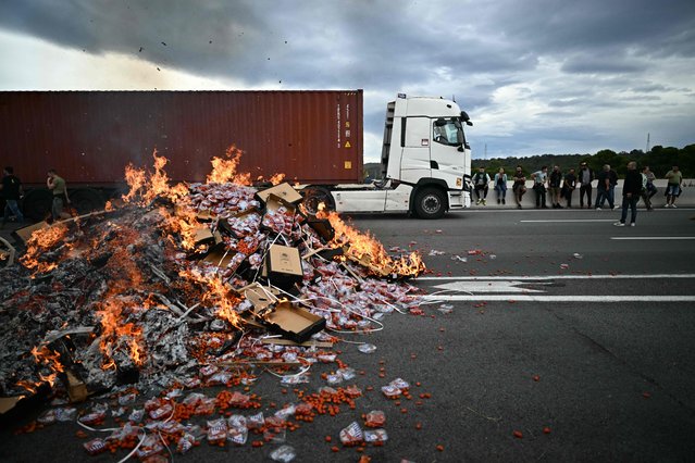 Protesters stand next to boxes of tomato burning in the road during a road blocking demonstration by winegrowers to protest against imports of Spanish wine, on the motorway at the toll booth of Le Boulou, close to the Spanish border, southern France, on October 19, 2023. Azerbaijan forces tightened their grip on the breakaway region of Nagorno-Karabakh on September 23, 2023, as international concern mounted over the plight of ethnic Armenian civilians trapped there. (Photo by Lionel Bonaventure/AFP Photo)