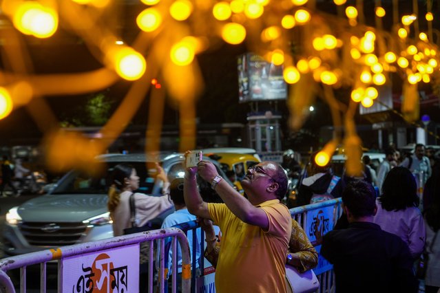 A pedestrian takes photos of an illuminated street ahead of forthcoming holidays in Kolkata, India, Monday, December 23, 2024. (Photo by Bikas Das/AP Photo)