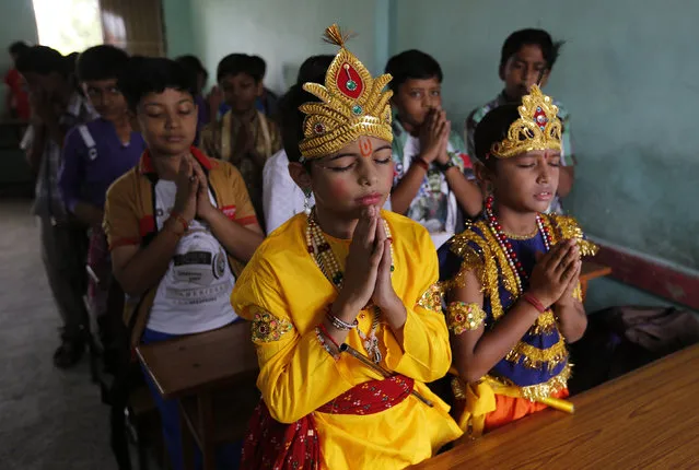 Students dressed as Lord Krishna (C) and his consort Radha (R) offer school prayers inside their classroom during celebrations marking the Janmashtami festival in Ahmedabad August 16, 2014. (Photo by Amit Dave/Reuters)