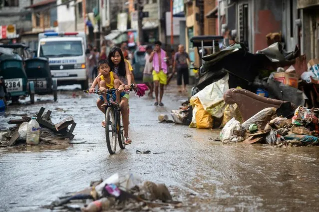 Children on a bicycle pass by debris from the flood caused by Super Typhoon Noru, in Marikina City, Metro Manila, Philippines on September 26, 2022. (Photo by Lisa Marie David/Reuters)