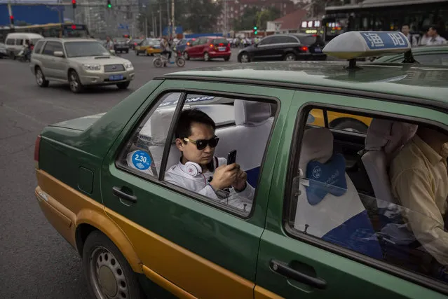 A Chinese man uses his smartphone as he sits in traffic in the back of a taxi on September 16, 2014 in Beijing, China. (Photo by Kevin Frayer/Getty Images)